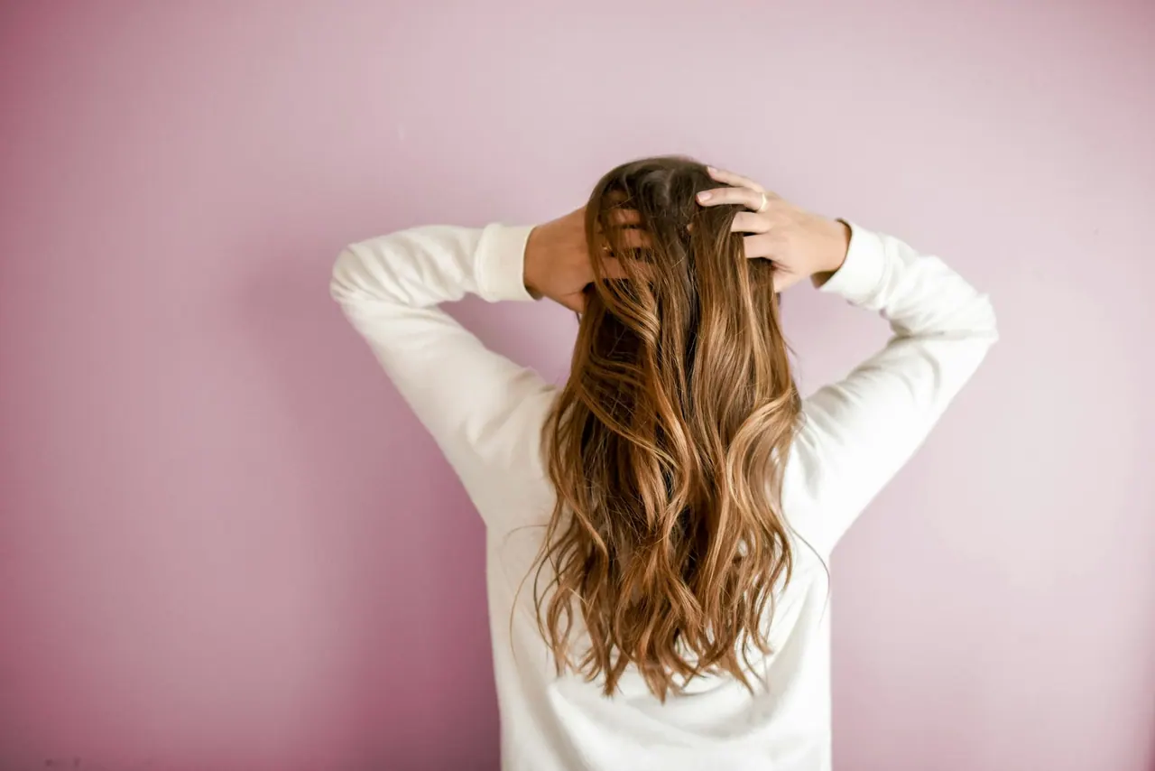 Long wavy balayage hair against a soft pink wall