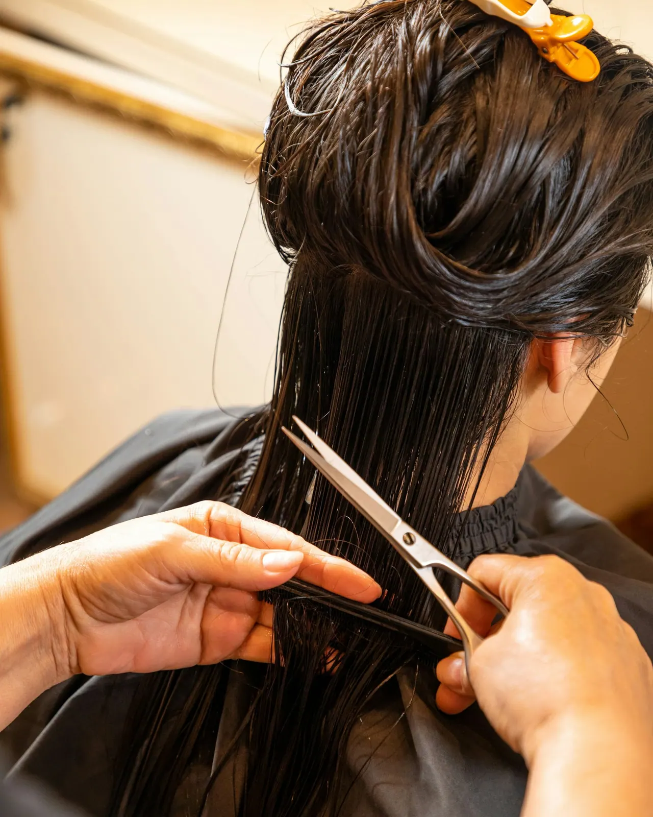 A stylist cutting long dark hair with scissors