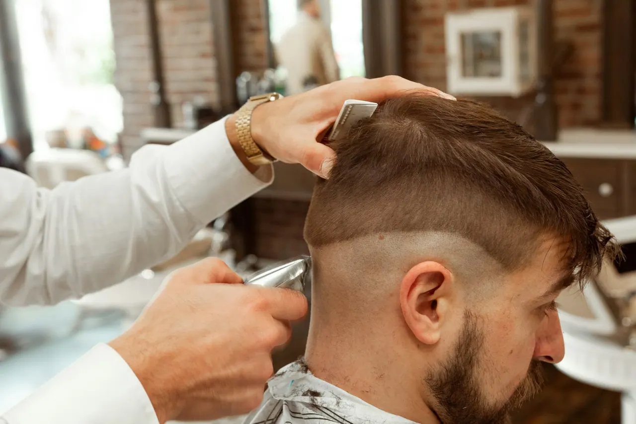 A barber cutting a skin fade with a clipper and a comb