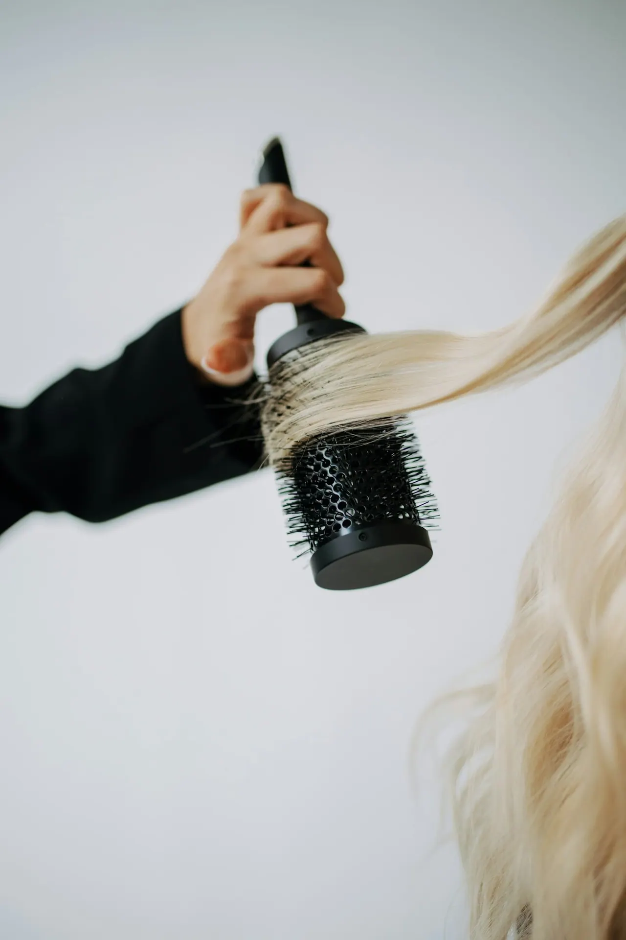 A round brush smoothing long, bright blonde hair