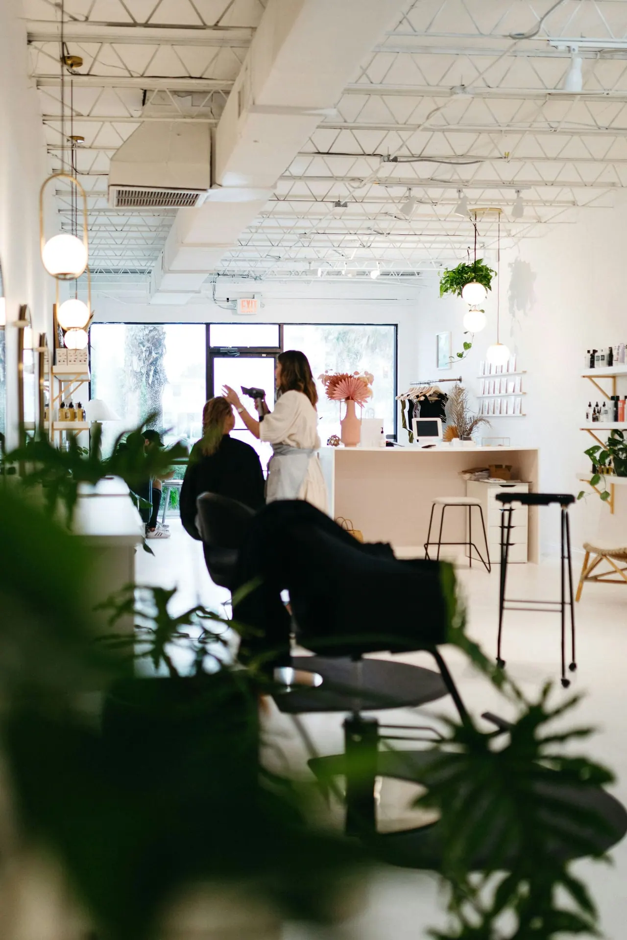 A bright salon full of plants and natural light, a stylist at work in the back