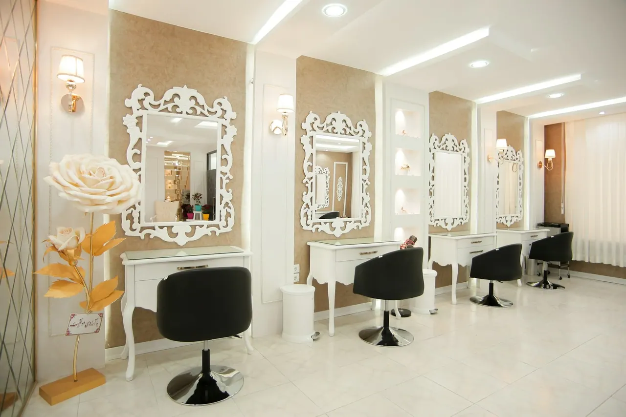 A bright salon with ornate white mirrors, soft lights and black styling chairs