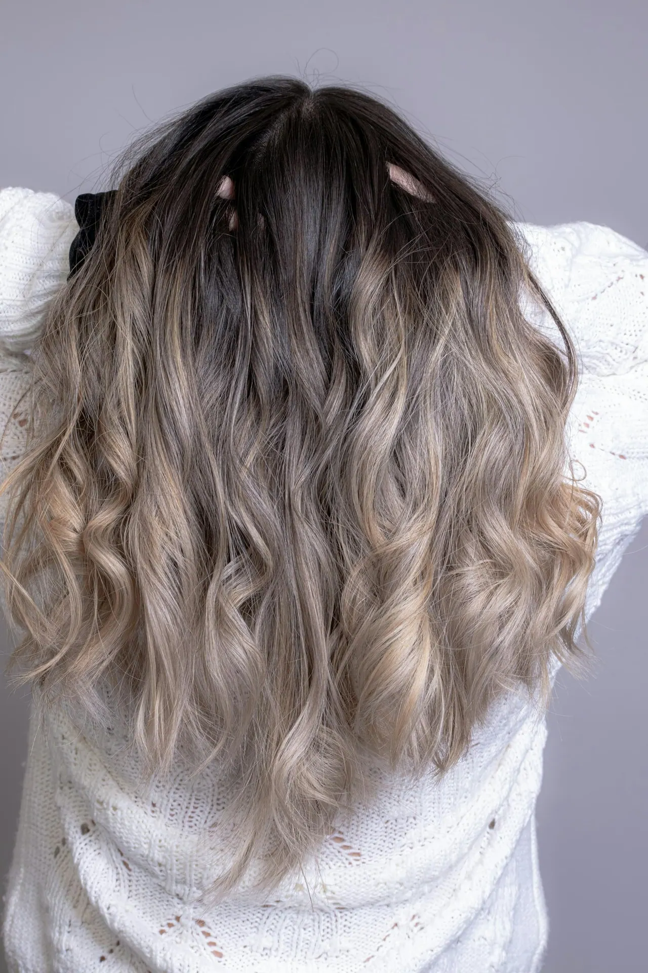 Long wavy balayage hair seen from behind, dark roots melting into soft ash blonde