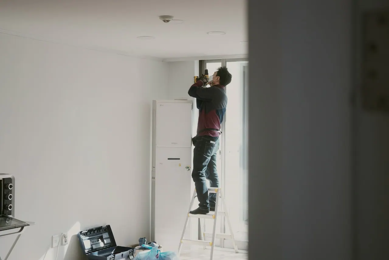 A handyman on a stepladder fixing a ceiling fitting in a bright room