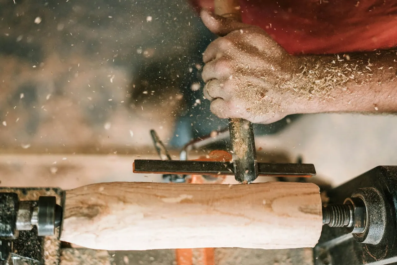 A woodworker's hand guiding a chisel on a turning spindle, shavings flying