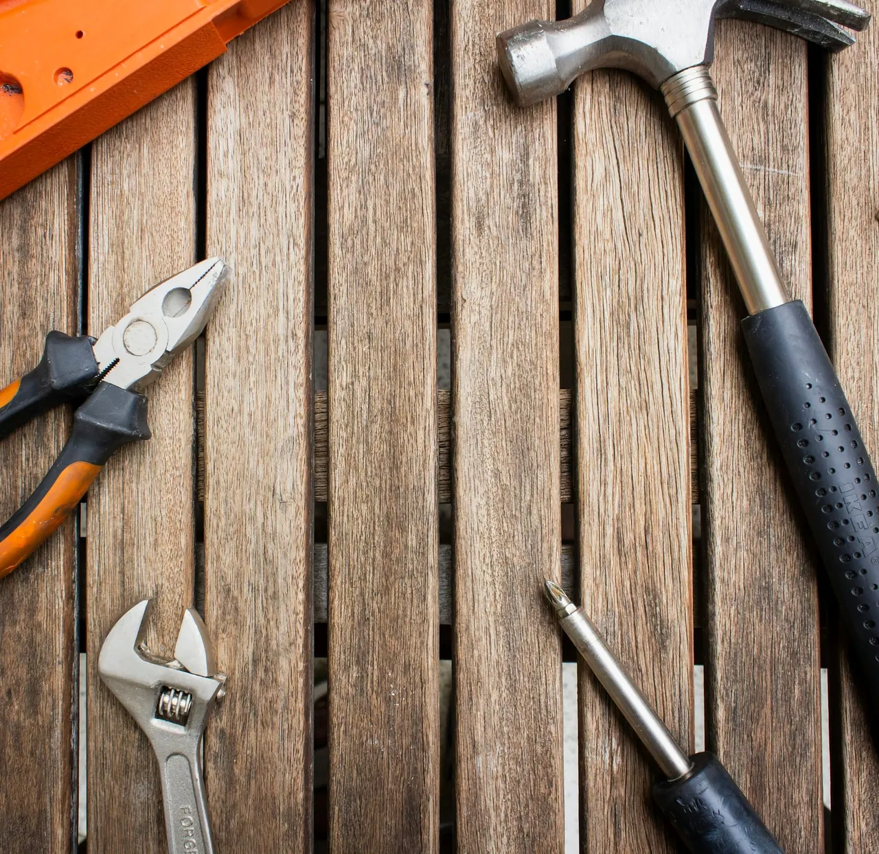 A hammer, pliers and a wrench laid out on a wooden table