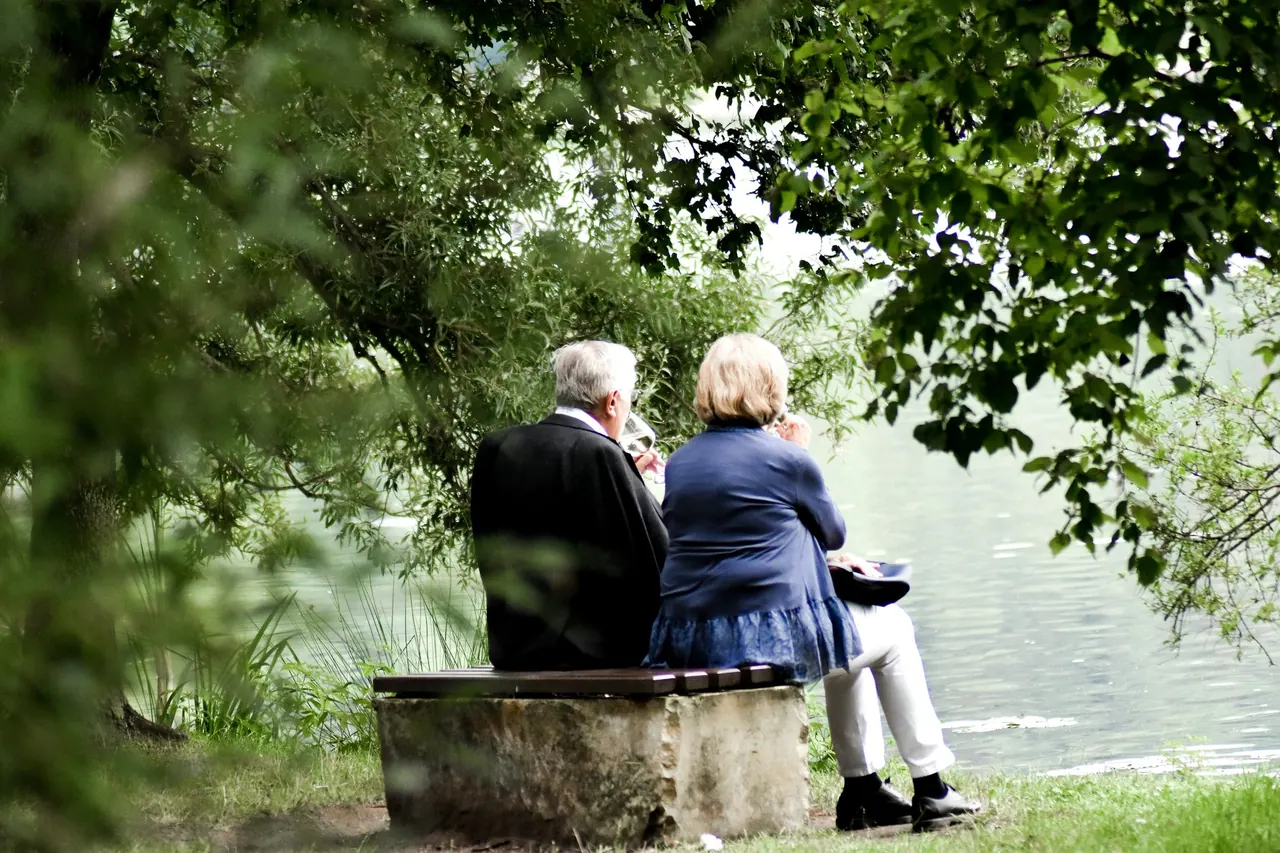 An older couple resting on a bench beside a lake