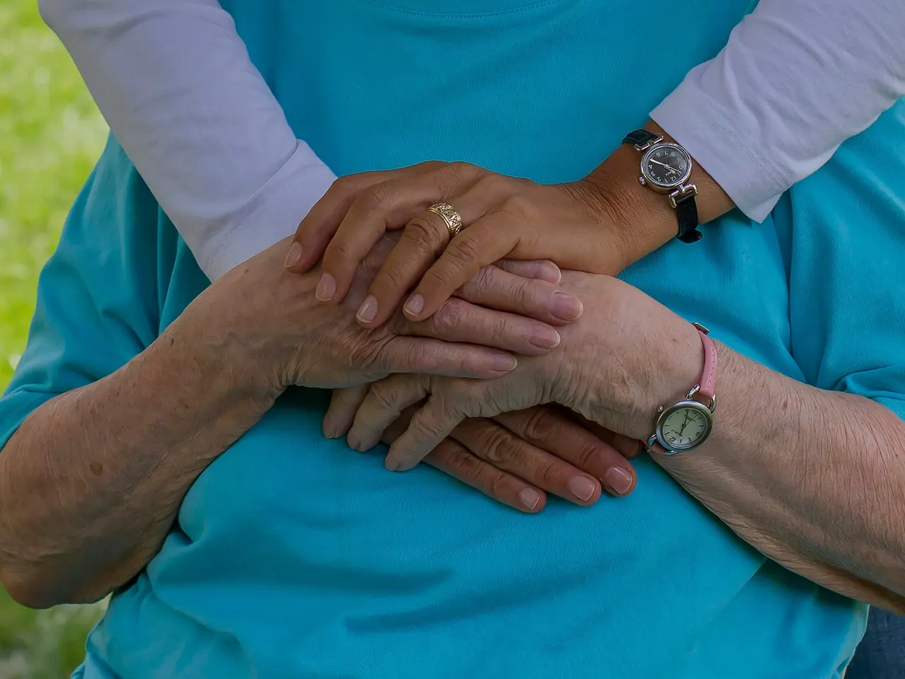 A caregiver’s hands resting gently on an older woman’s hands