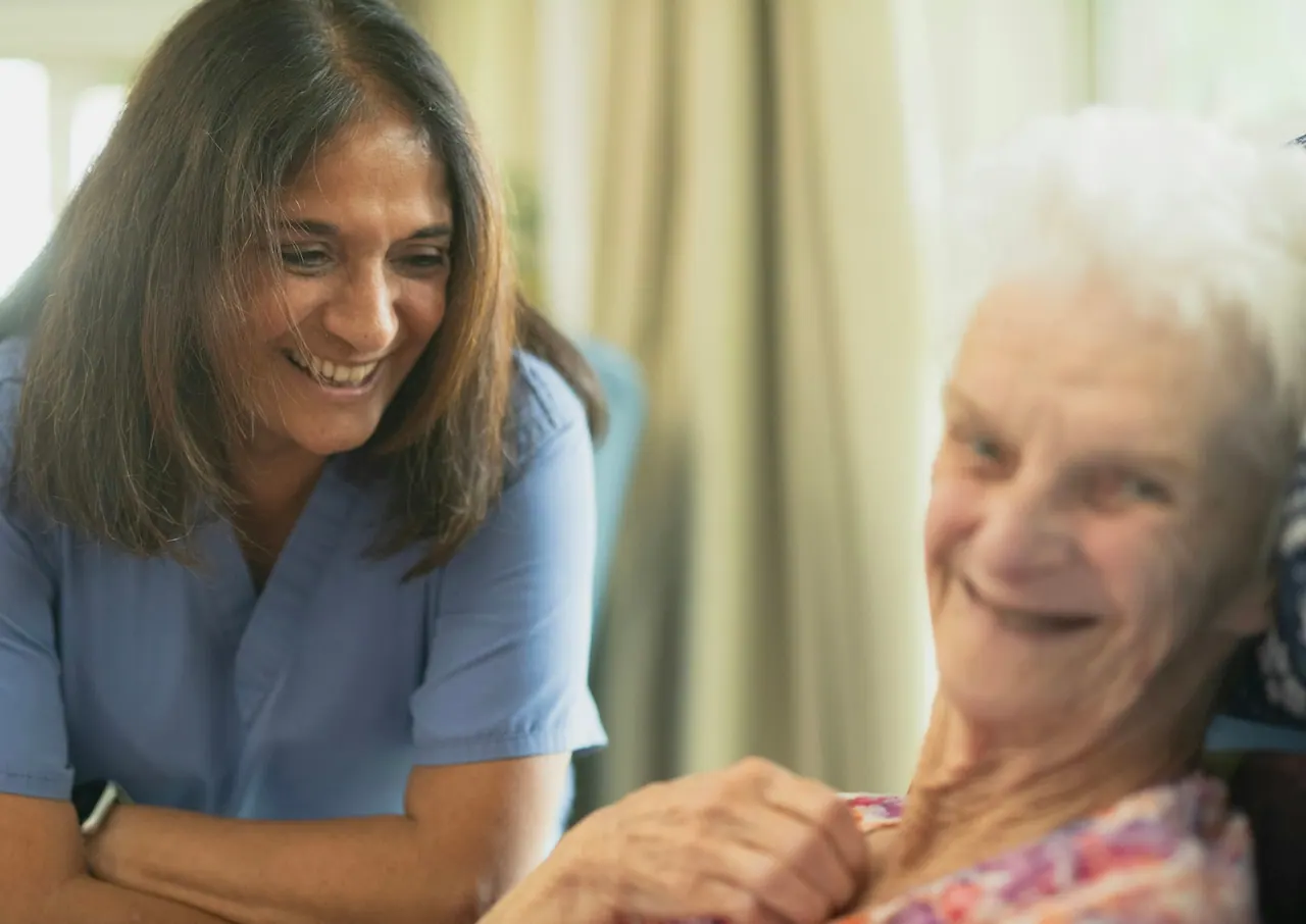 A caregiver sharing a warm laugh with an older woman at home