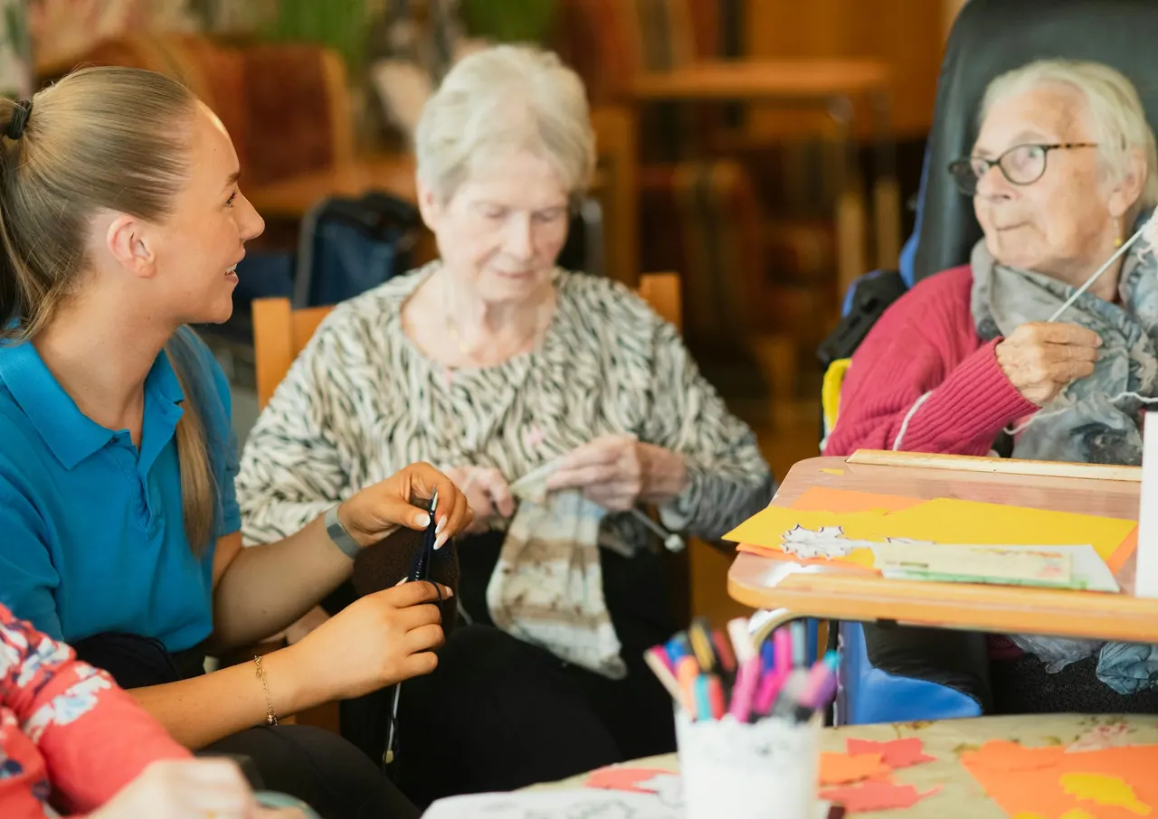 A caregiver chatting with two older women who are knitting