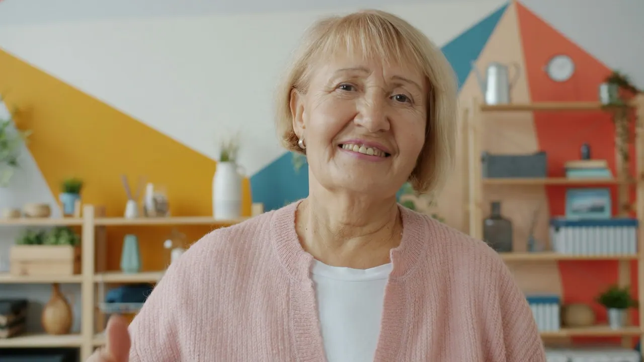 A smiling older woman in a pink cardigan at home