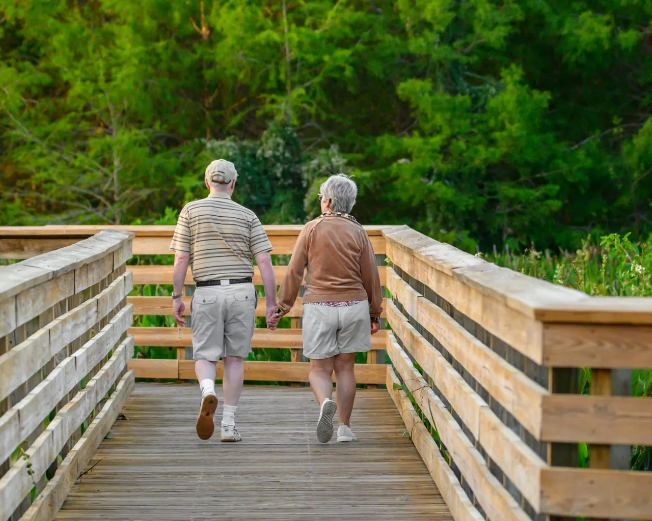 An older couple walking hand in hand along a wooden boardwalk