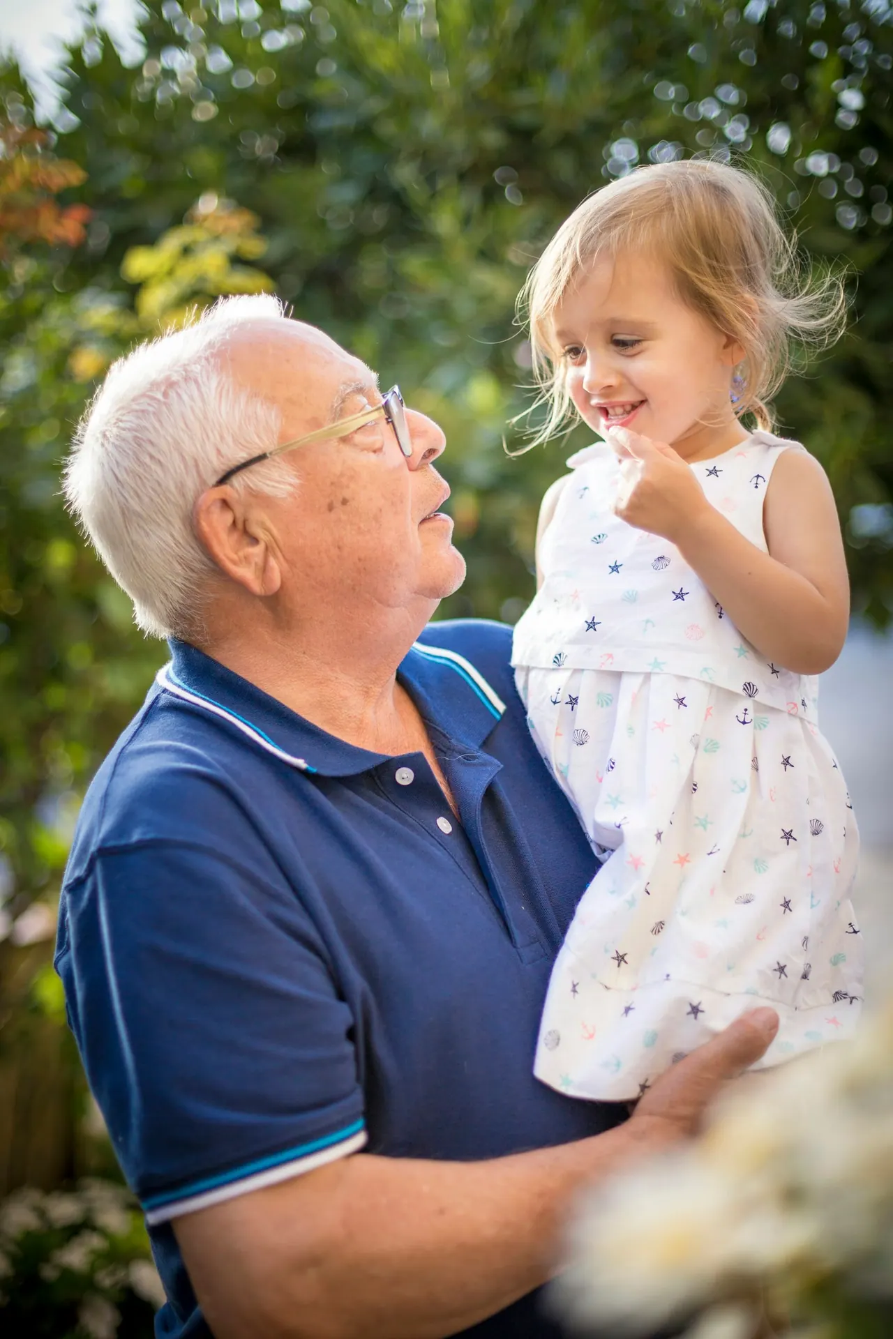 A grandfather laughing with his little granddaughter in the garden