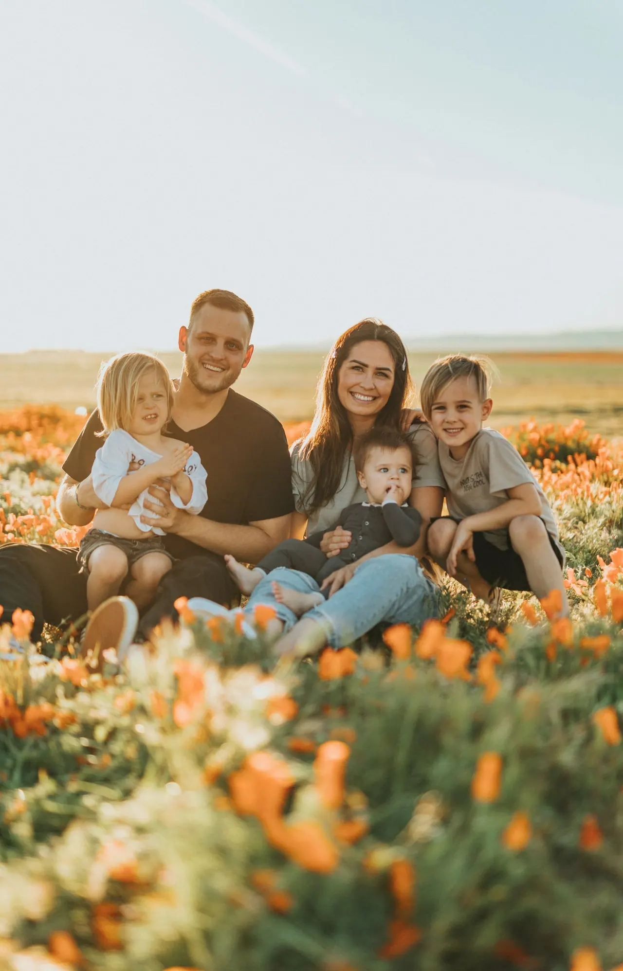 A family of five smiling in a field of orange poppies