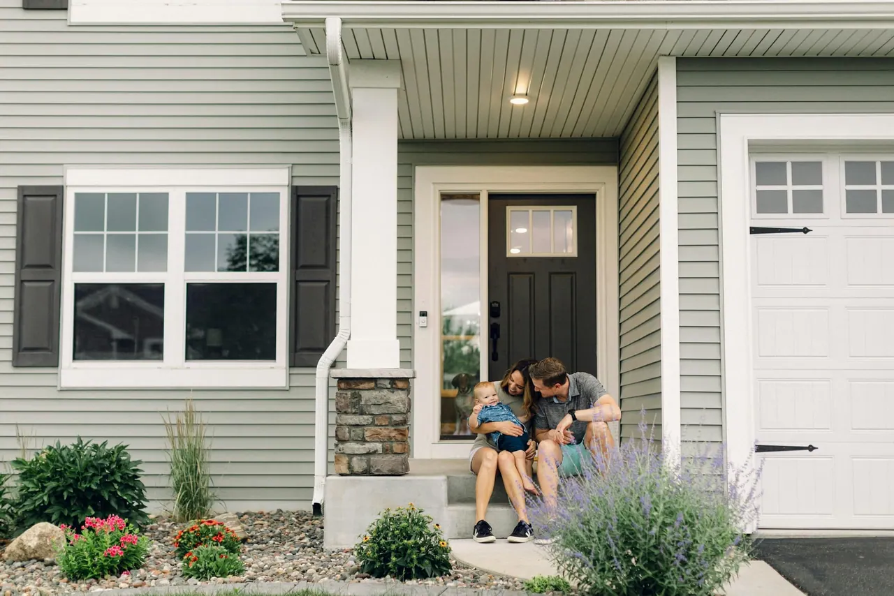 A young family sitting together on the front steps of their home