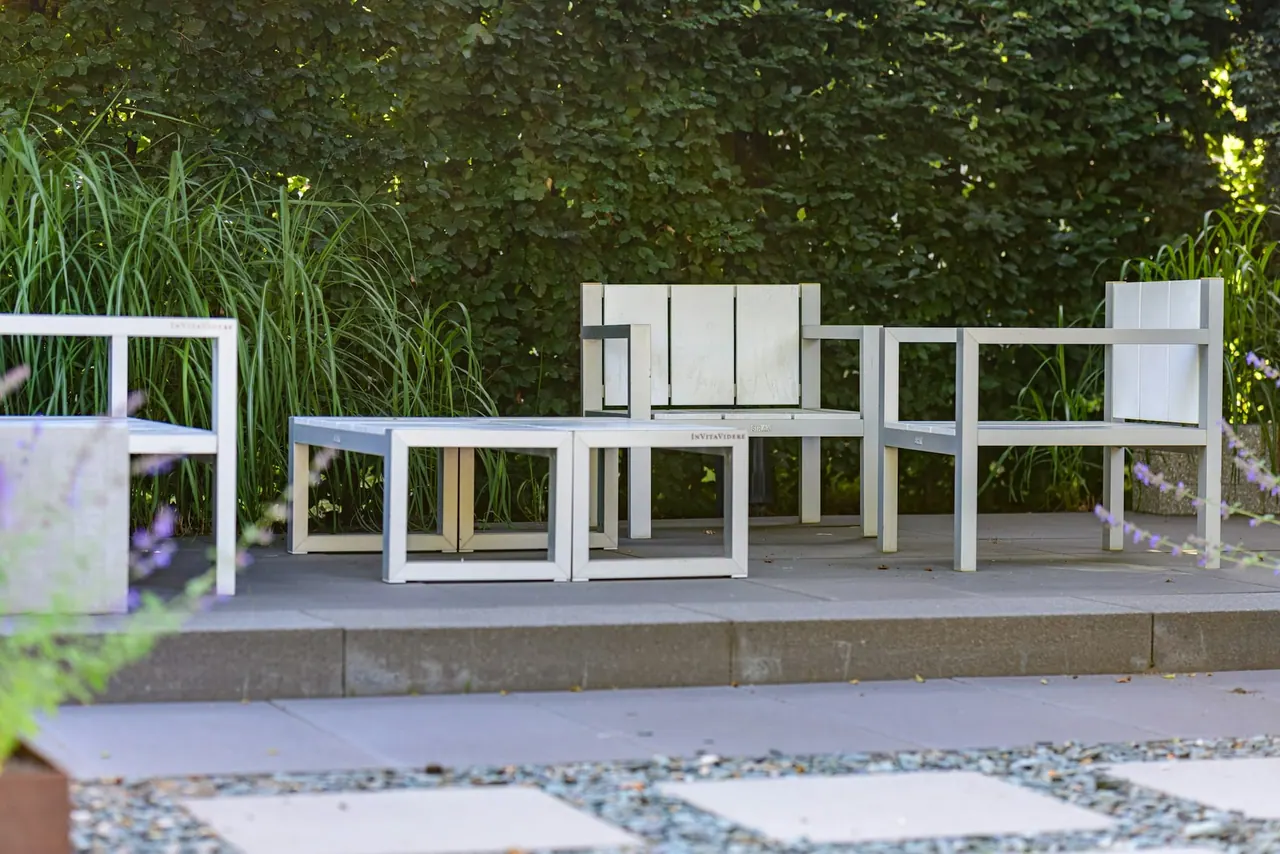 A pale stone courtyard with white outdoor chairs against a green hedge