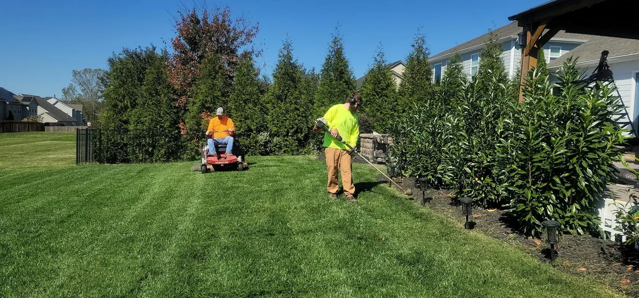 Two crew members mowing and trimming a large green lawn