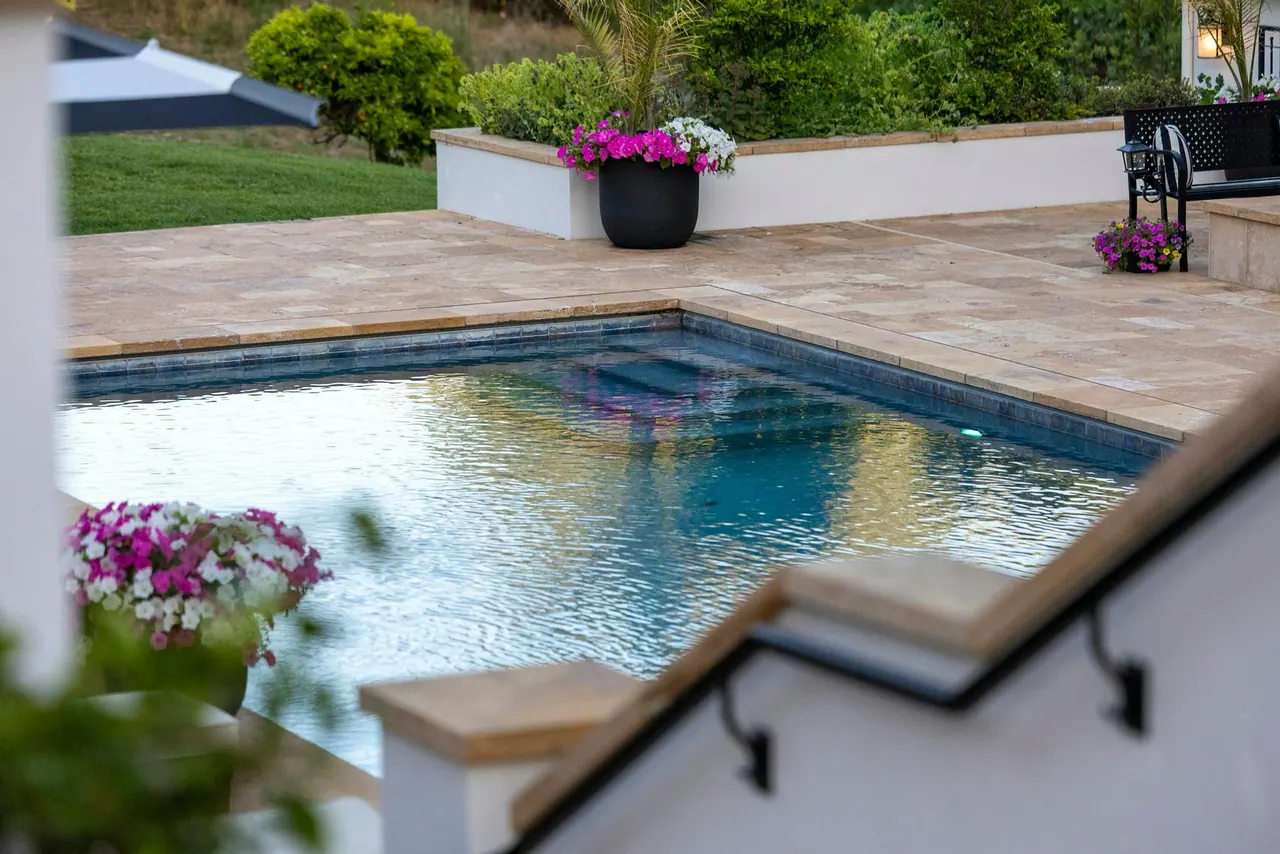 A swimming pool with a stone deck, steps and potted flowers