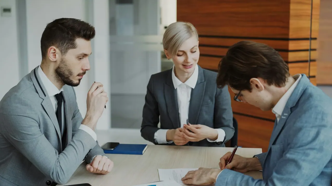 A lawyer smiling as two clients sign an agreement at a table