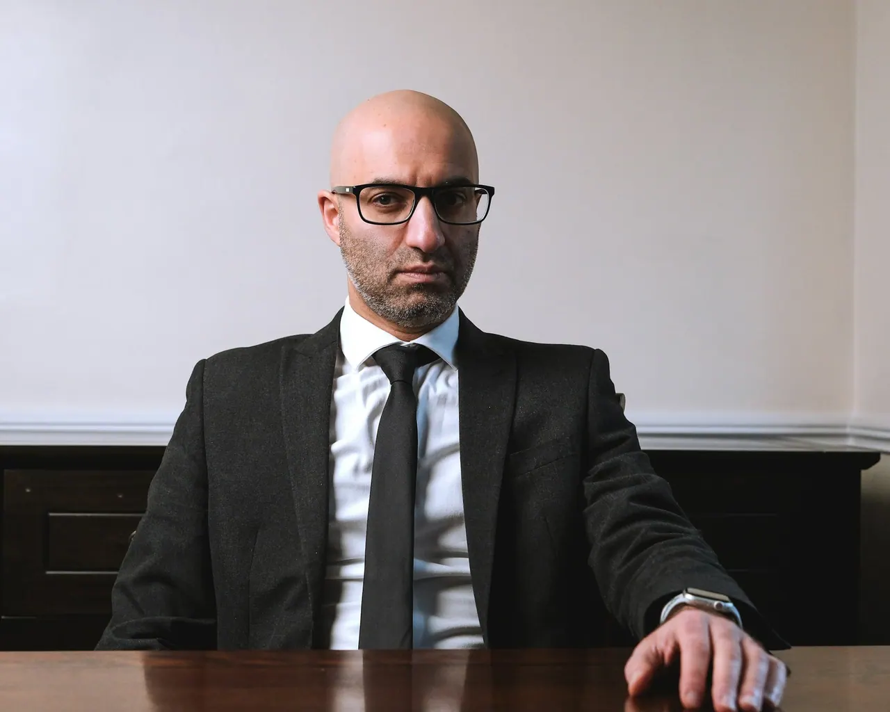 A partner in a dark suit and glasses seated at a polished table