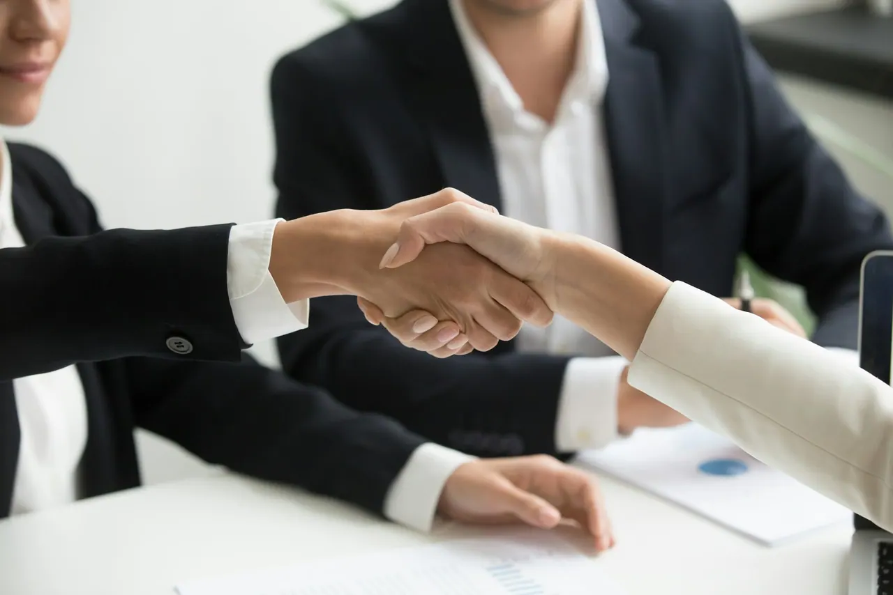 Two people shaking hands across a desk after signing