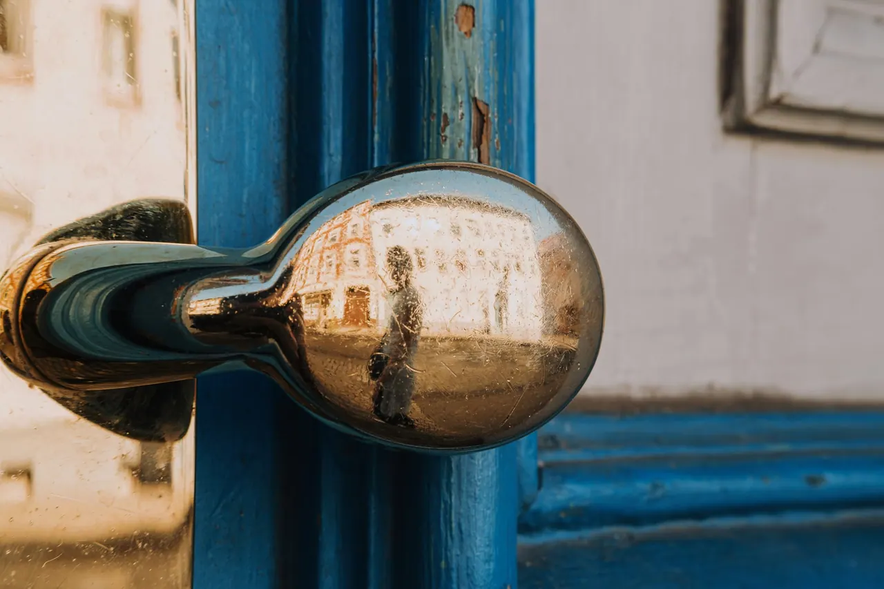 A chrome door knob on a blue door, reflecting the street