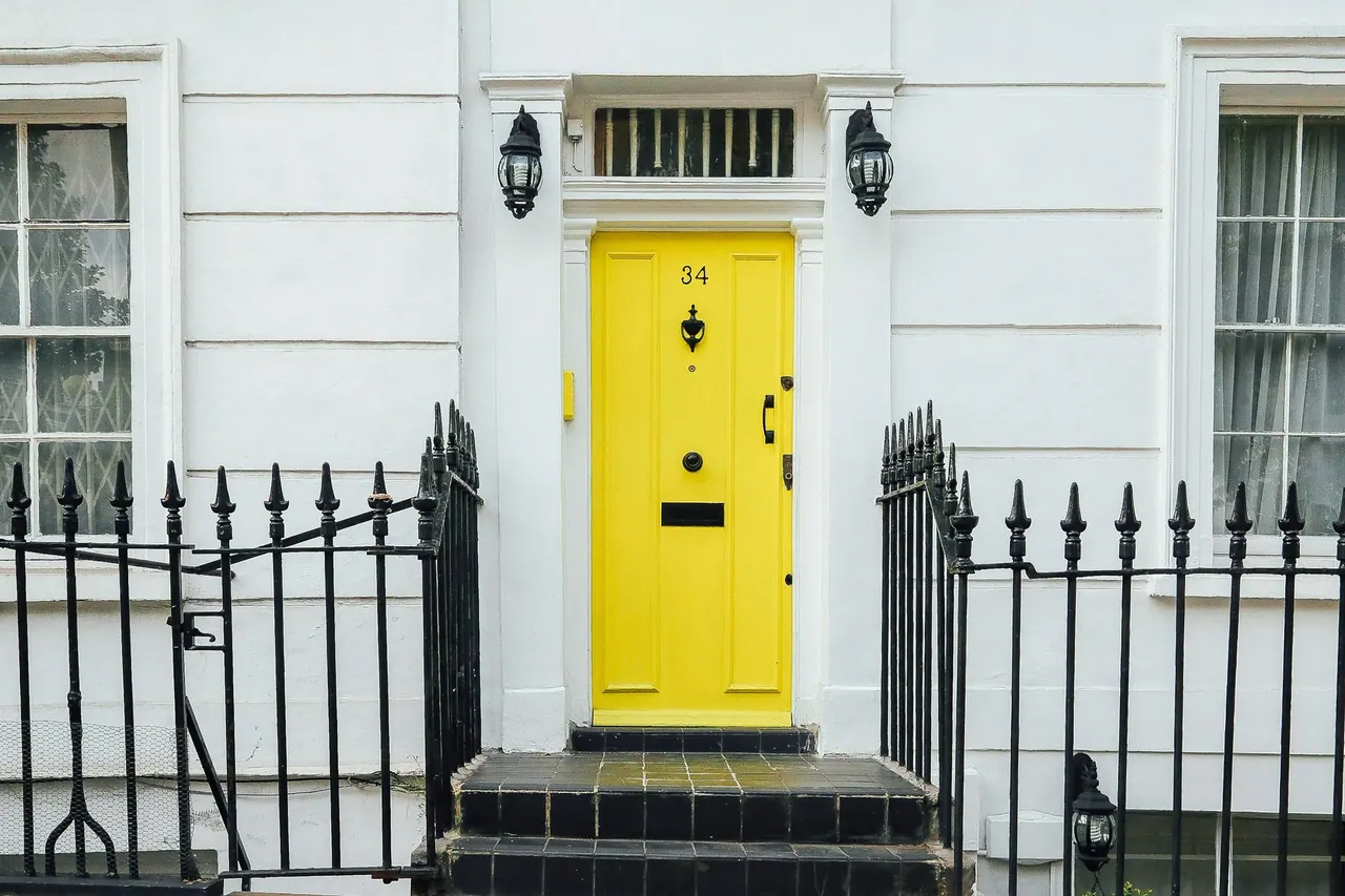 A bright yellow front door behind black iron railings on a white terrace