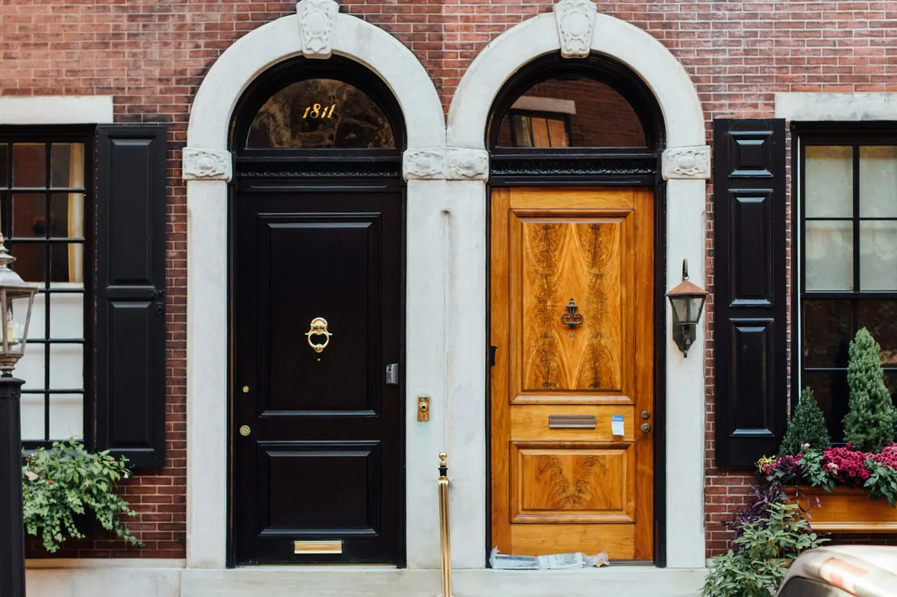 Two front doors, one black and one oak, under white stone arches in a brick terrace