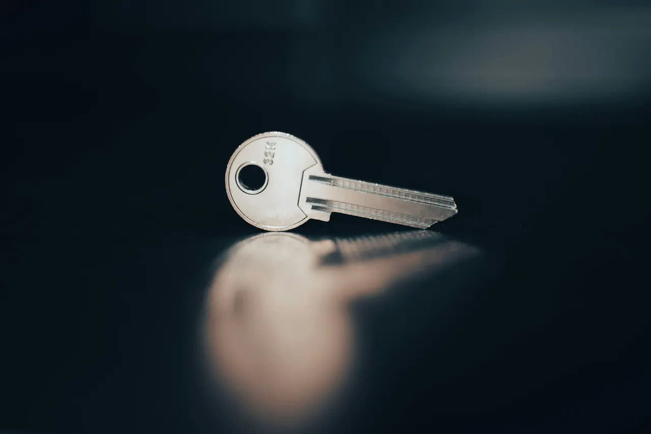 A single silver key lying on a dark blue surface