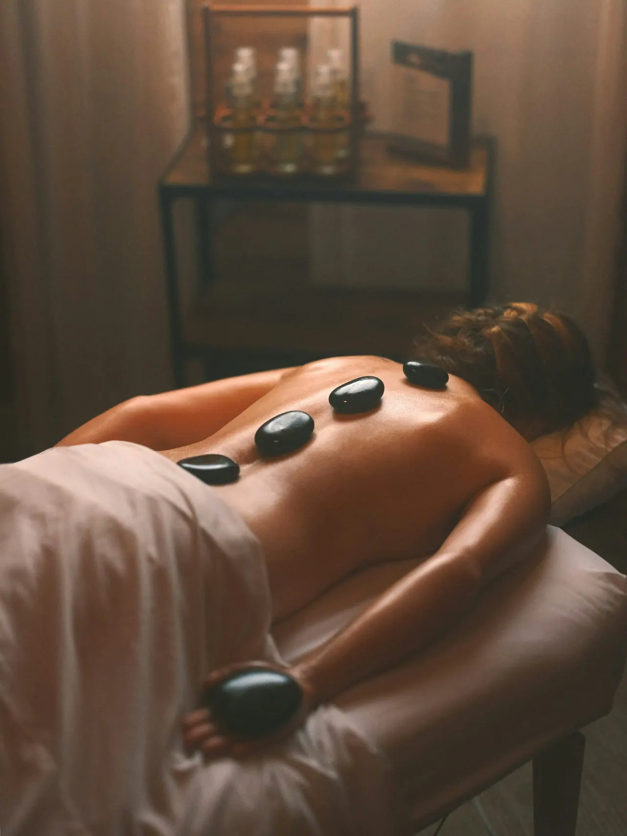 Warm black stones resting along a client’s back in a dim room