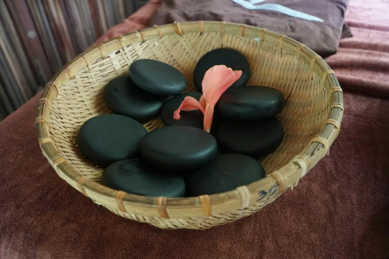 A woven basket of smooth black massage stones with a flower