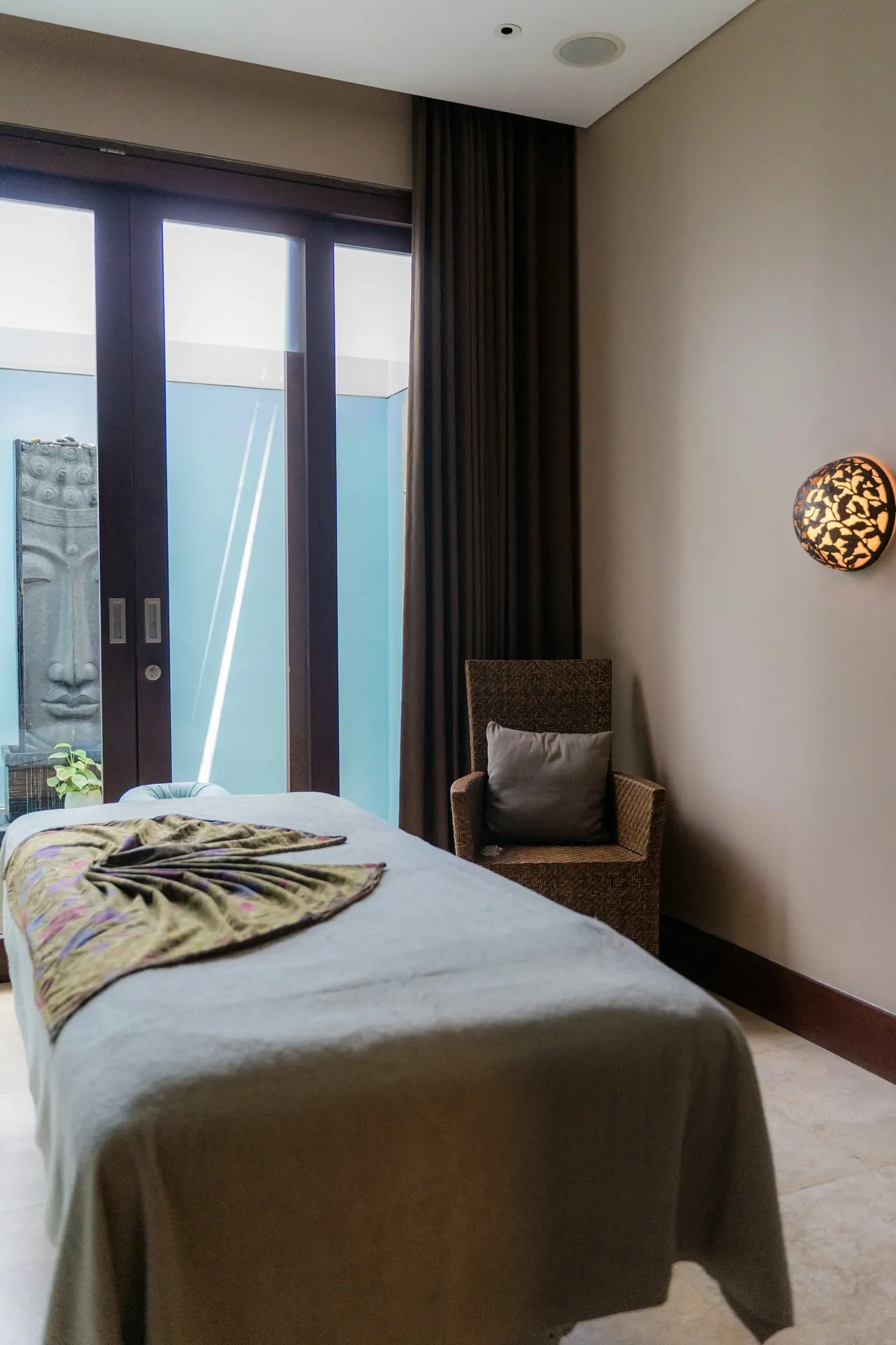 A quiet treatment room with a made massage table by a tall window