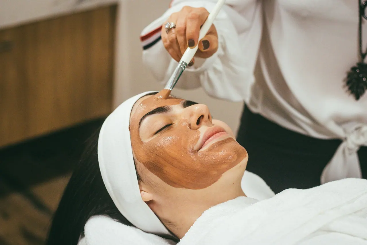 An esthetician brushing a clay mask onto a relaxed guest