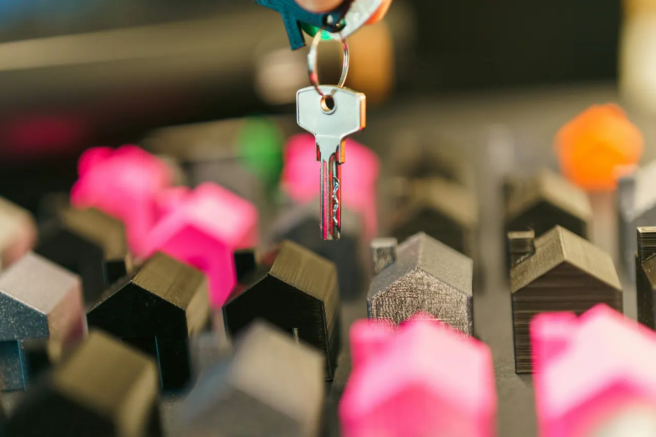 A hand holding a house key above rows of small model houses