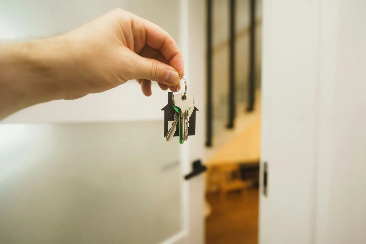 A hand holding a house key up to an open front door