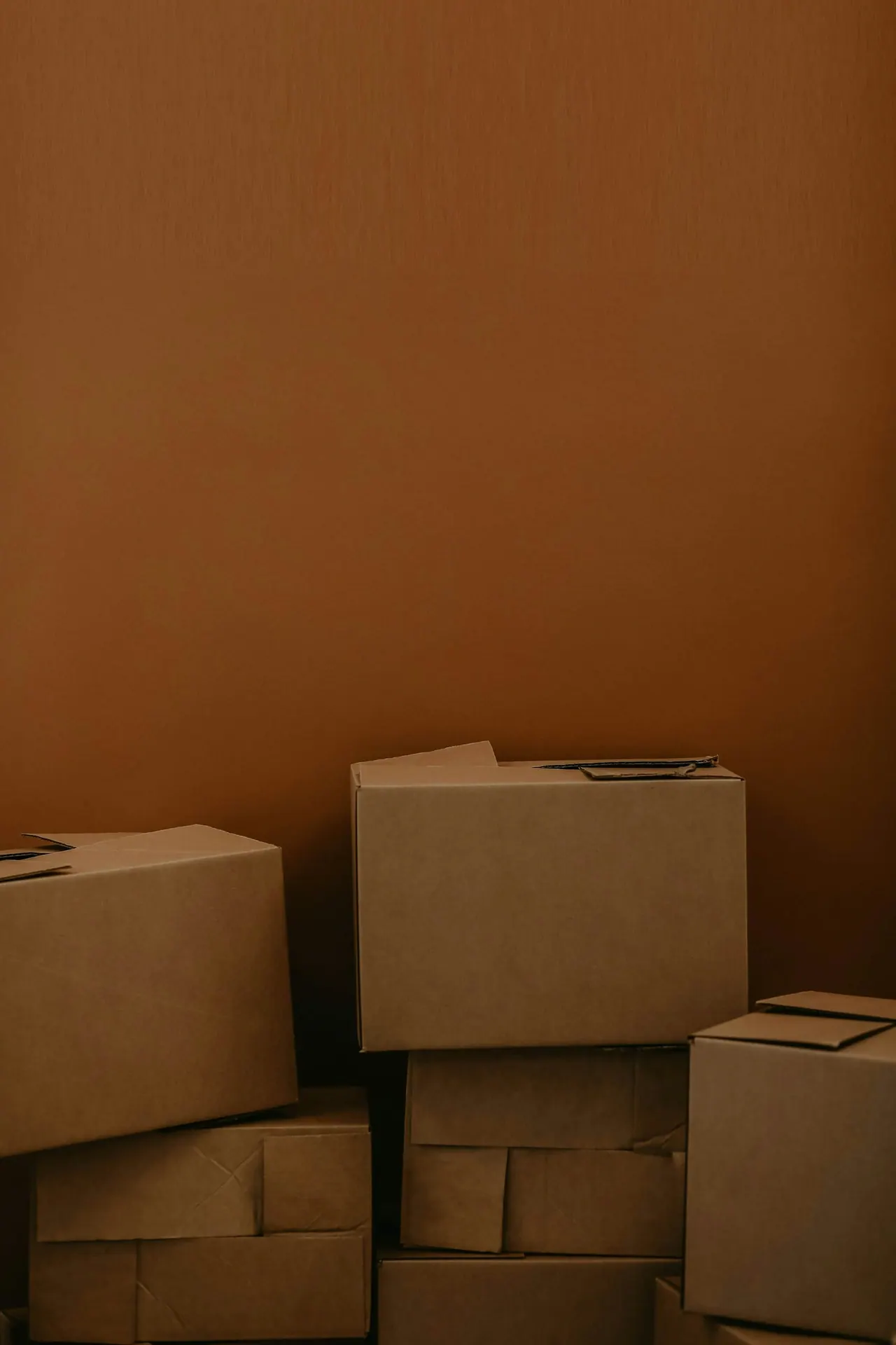 A neat stack of cardboard moving boxes against a warm brown wall