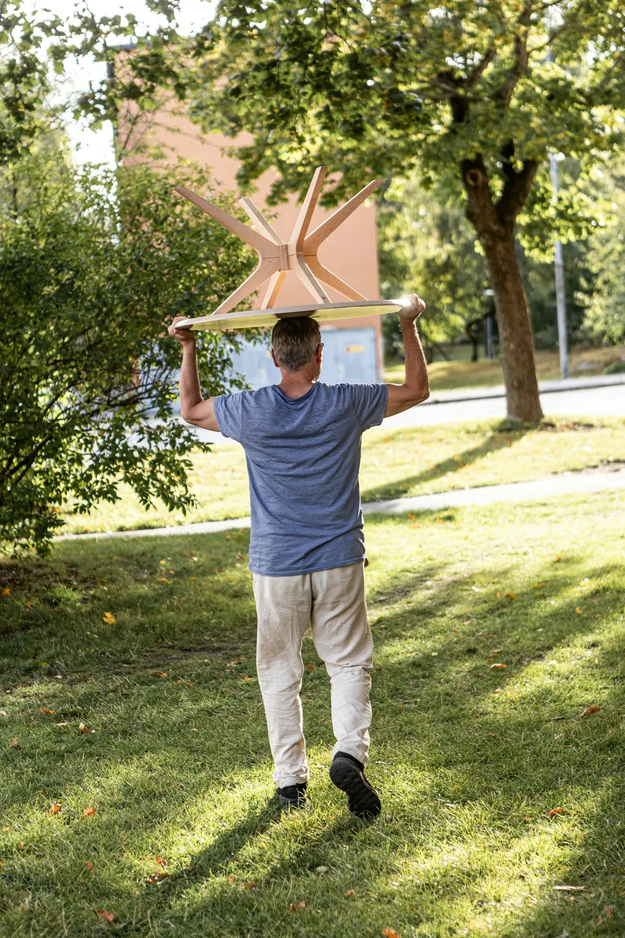 A mover carrying a wooden table across a sunny garden