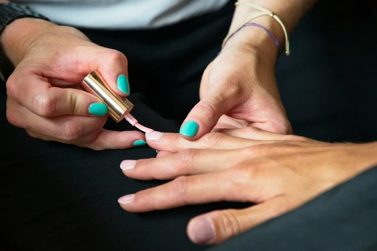 A technician brushing pale pink polish onto a client’s nails