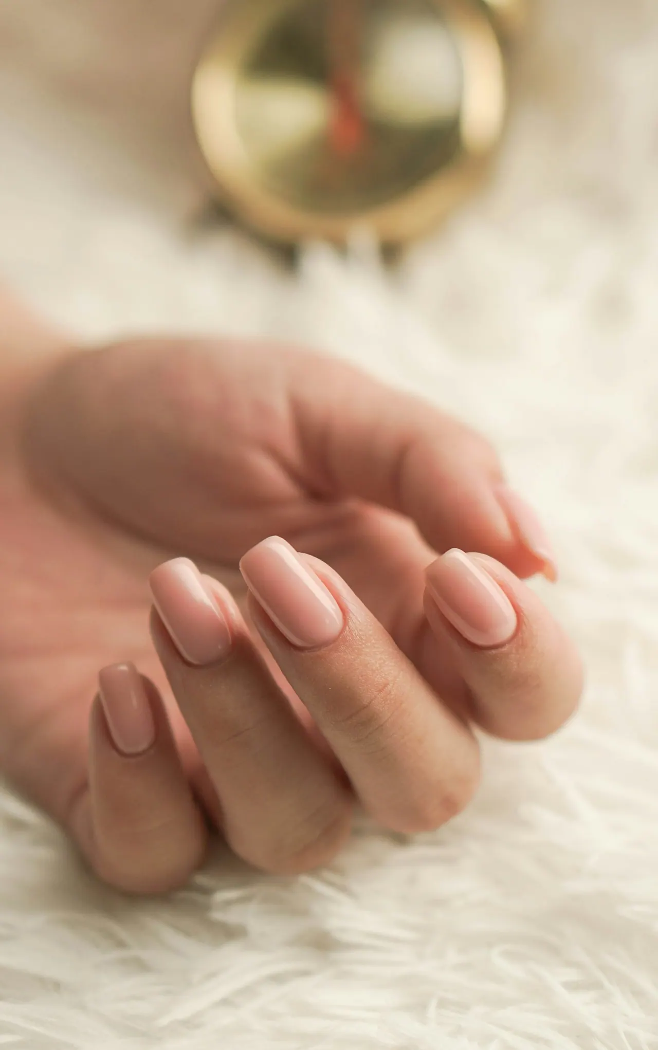 A relaxed hand with soft pink nails on white fluff