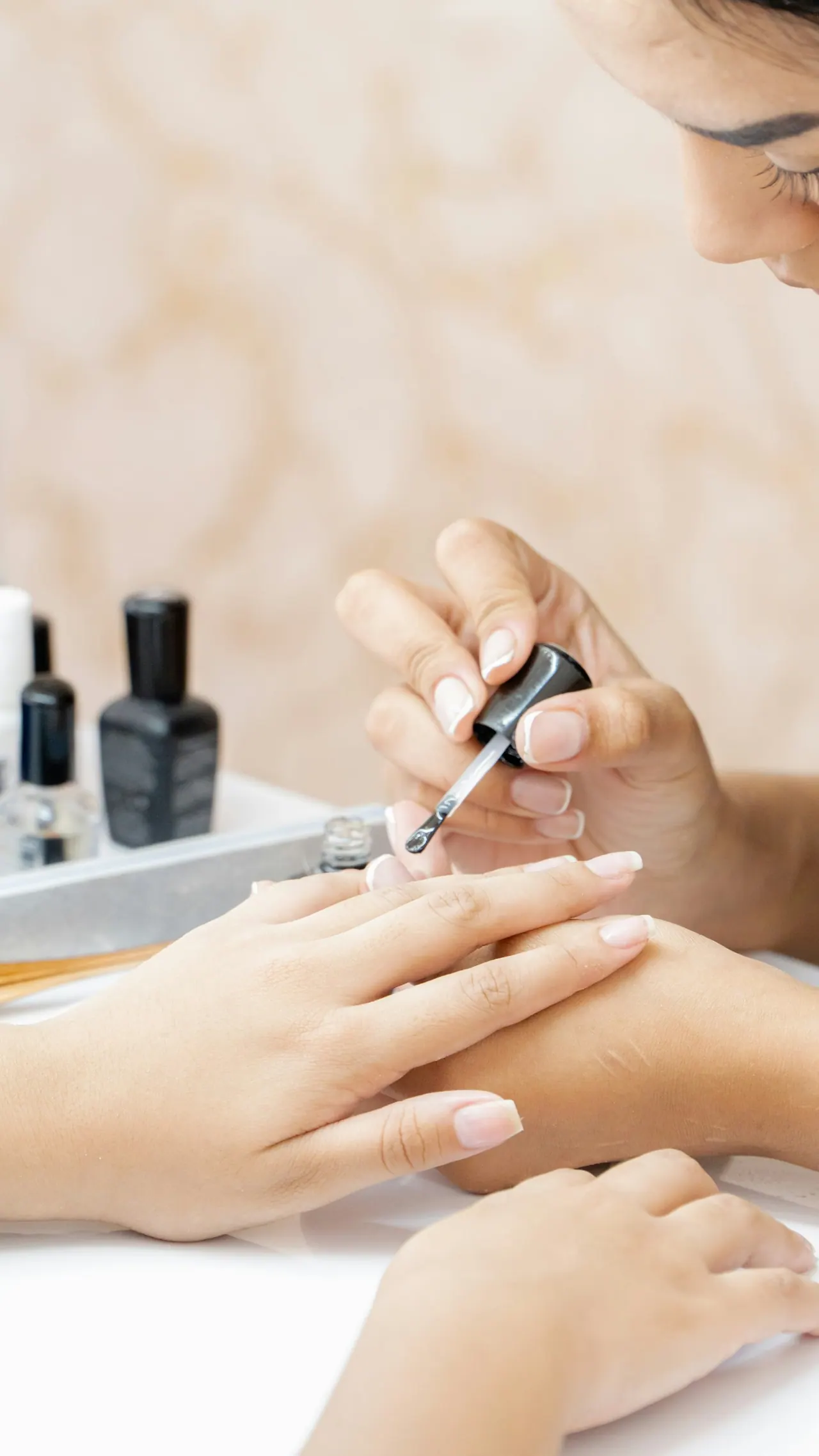 A technician painting a client’s nails a soft nude