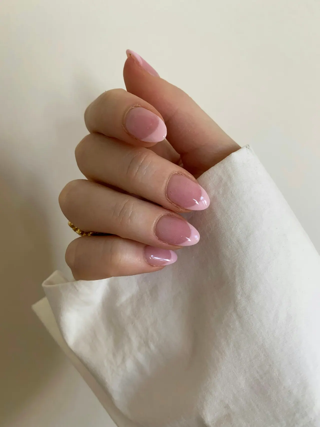 A hand with glossy pink almond gel nails holding white linen