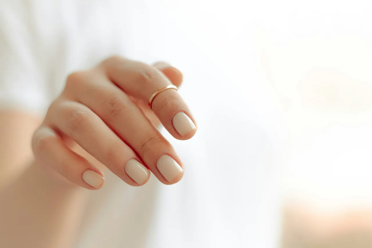 A hand with glossy cream nails and a fine gold ring