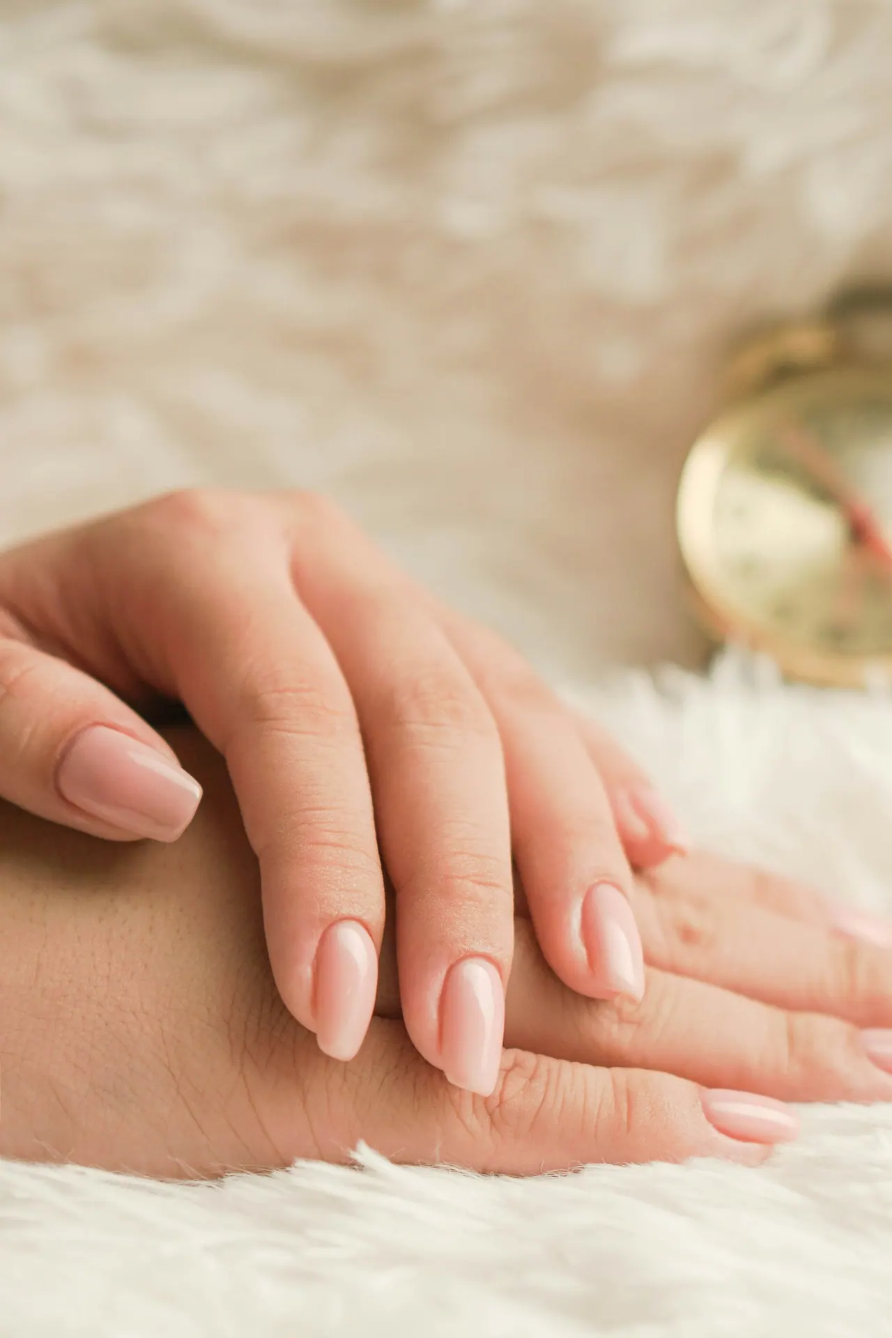 Hands with nude nails resting on soft fur beside a gold clock