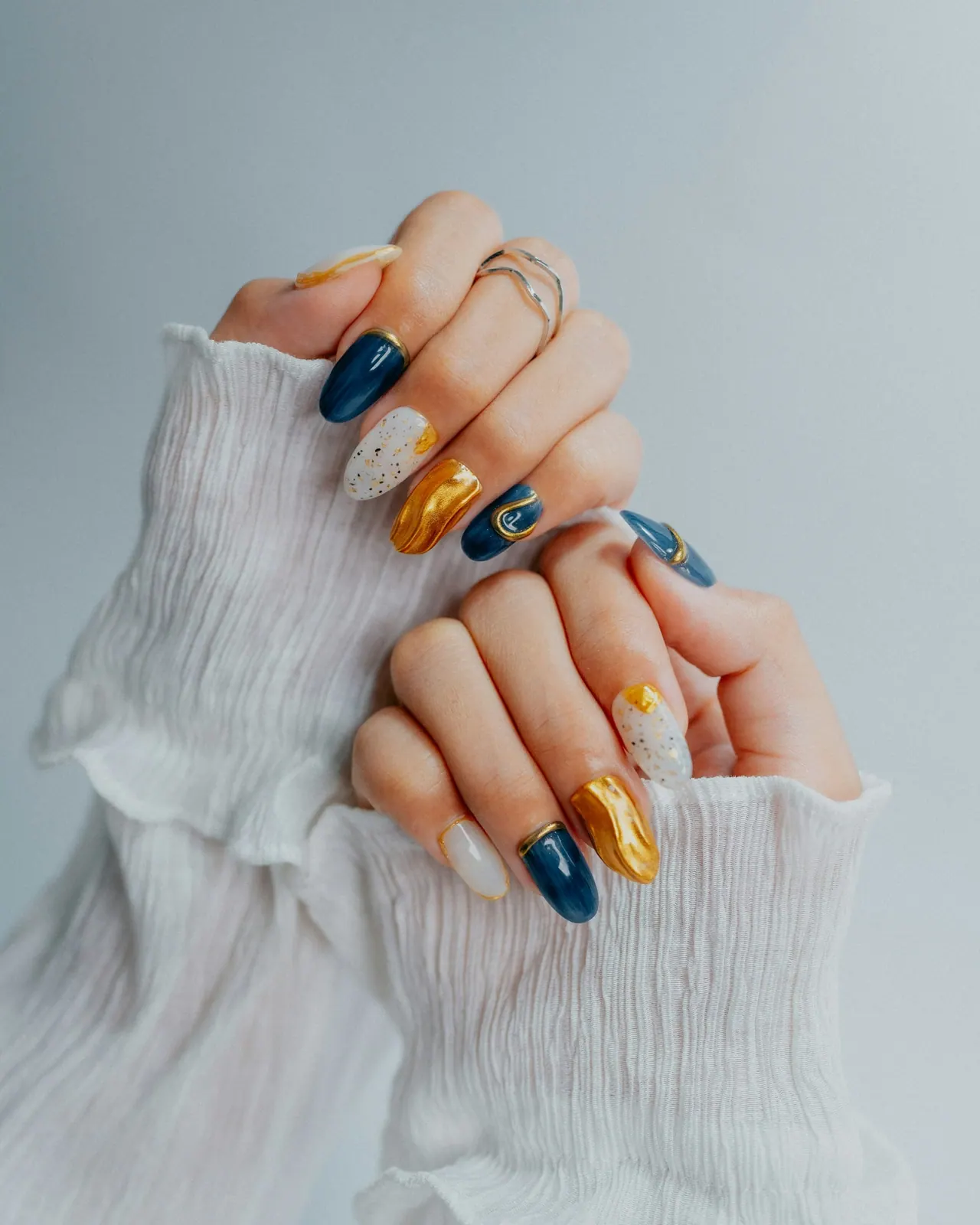 Hands with navy, gold and white nail art holding a white ruffled sleeve