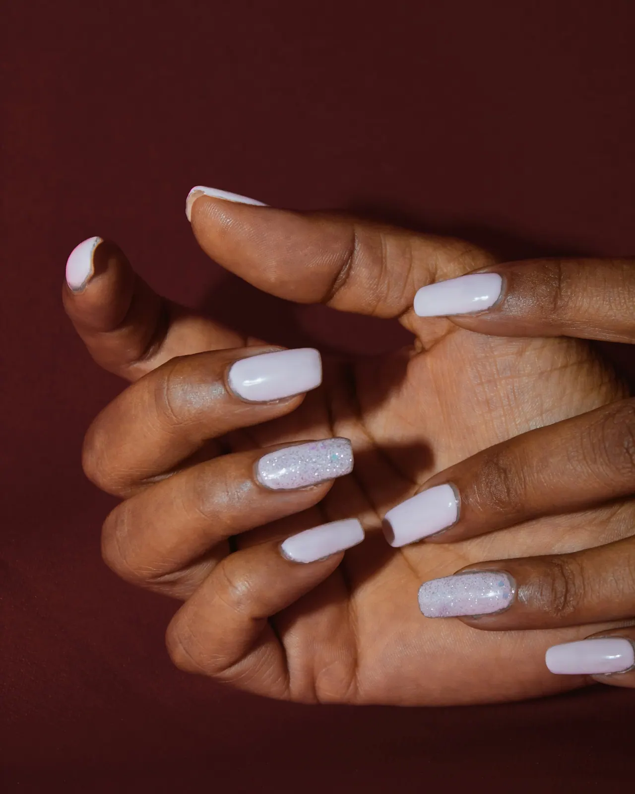 Hands with milky white nails against deep burgundy