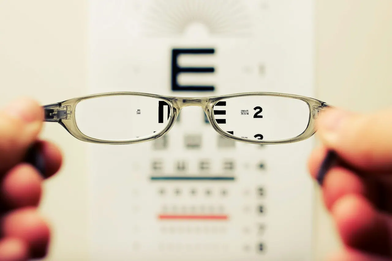 A pair of glasses held up in front of an eye chart, the letters sharp through the lenses