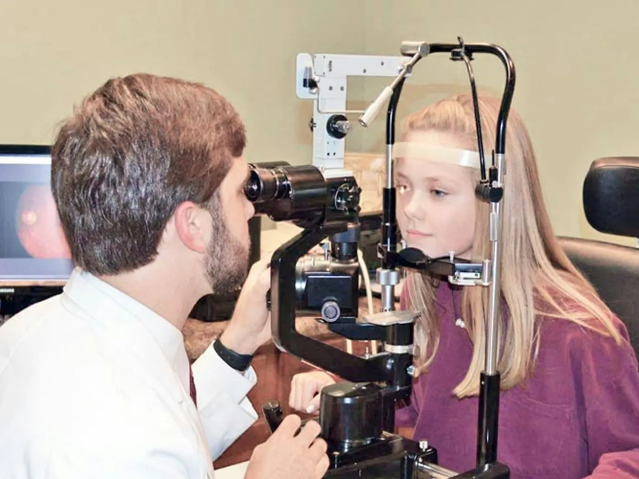 An optometrist examining a young girl’s eyes with a slit lamp