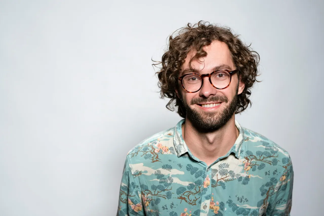 A smiling man with curly hair in round tortoiseshell glasses