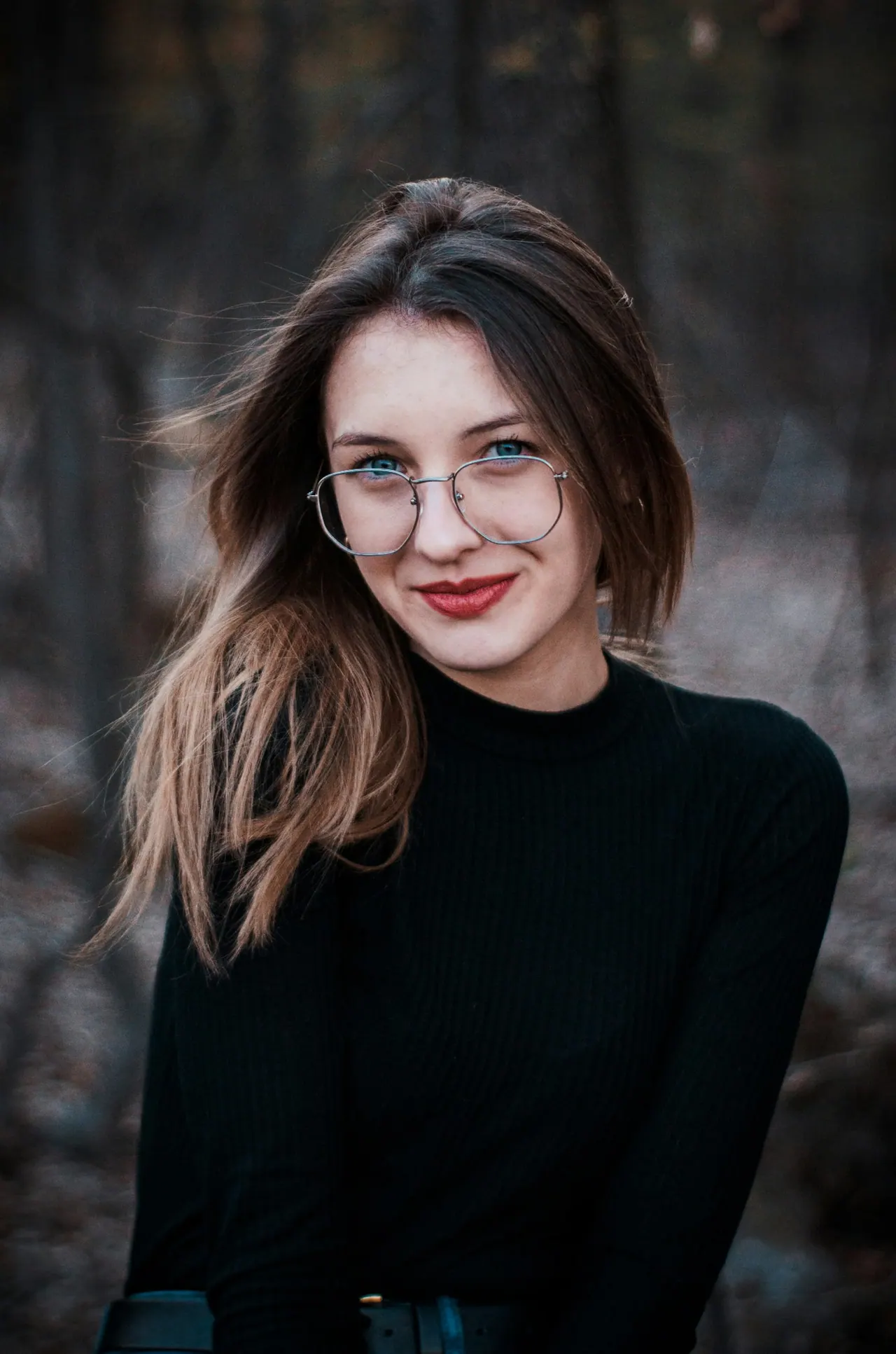 A young woman in clear framed glasses smiling outdoors