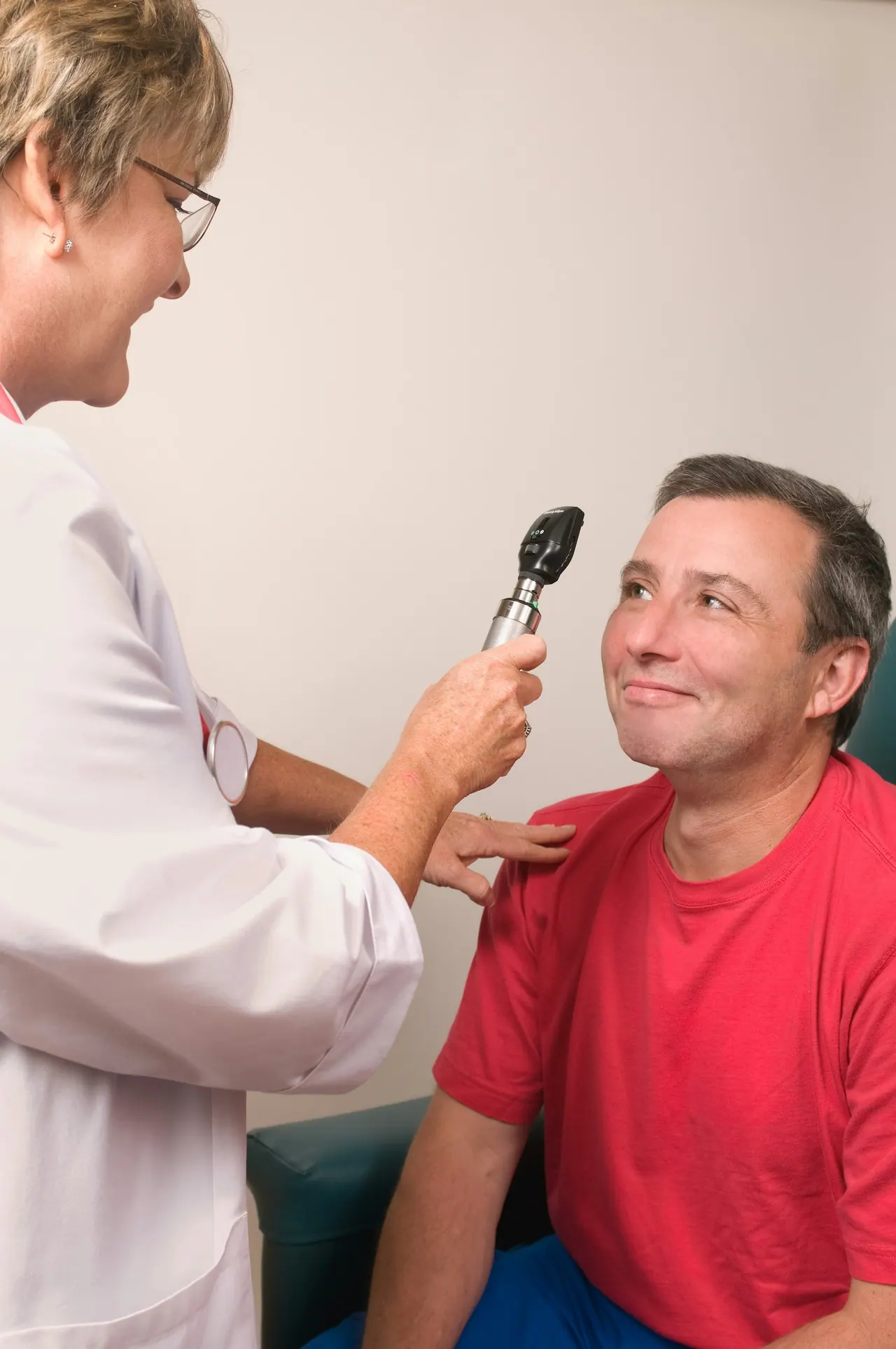 An optometrist checking a smiling man’s eyes with a handheld light